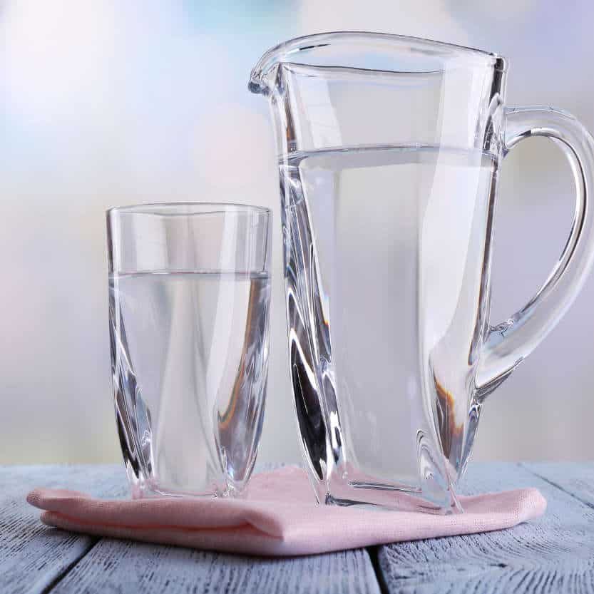 Glass pitcher and glass of water on wooden table on bright background. The water was purified via a reverse osmosis system for drinking water in Chandler AZ